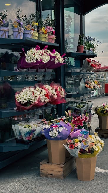 A display of florist arrangements at Sidcup Florist, showcasing a variety of fresh flowers including white chrysanthemums, pink lilies, and red roses, wrapped in colorful paper and placed in paper and